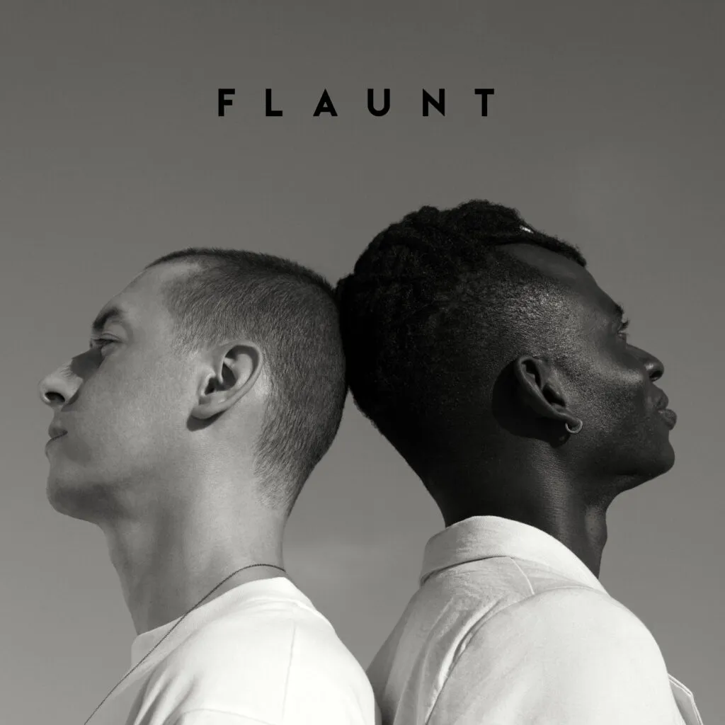 A black-and-white image of two individuals standing back-to-back, representing contrast and unity, with the word "FLAUNT" displayed above them.