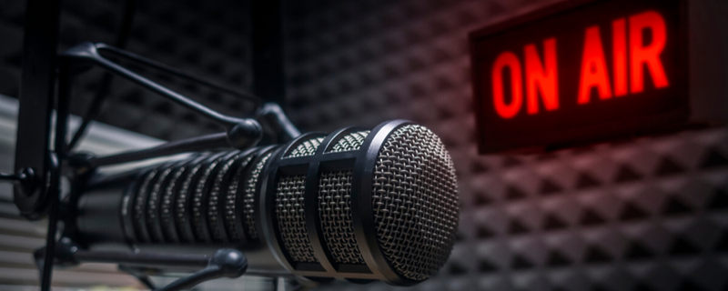 A professional studio microphone in front of a red "ON AIR" sign, symbolizing live radio broadcasting and music promotion.