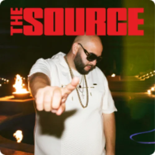 A hip-hop artist wearing sunglasses and a gold chain, pointing towards the camera with a confident pose, under The Source magazine logo, with fire-lit scenery in the background.