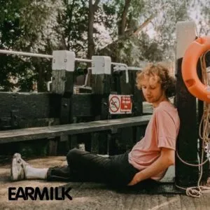 An independent artist sits thoughtfully near a dock, embodying the introspective and creative journey of musicians growing their audience through TMMA’s strategic music marketing and Spotify promotion.